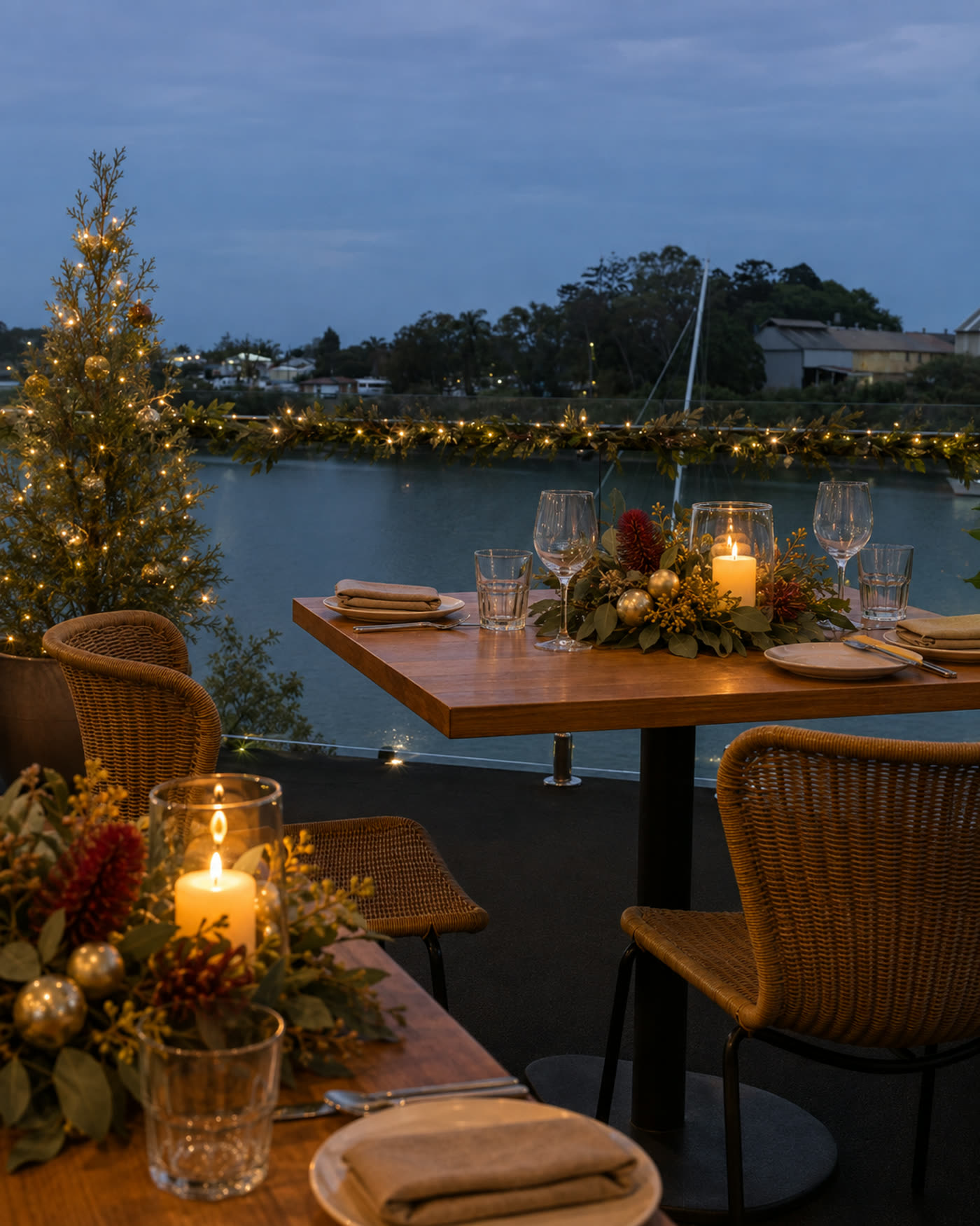 A table on the deck at Burnett Riverside dressed for Christmas in red and gold, with the river behind at dusk