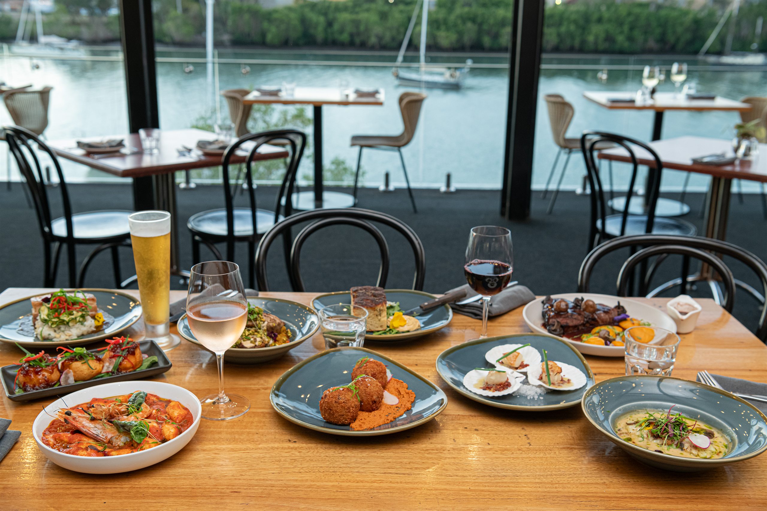 Shared plates and drinks on a table at H2O, with the Burnett River behind